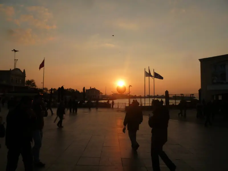 The sun setting over the water from the Kadıköy promenade, a ferry on the horizon
