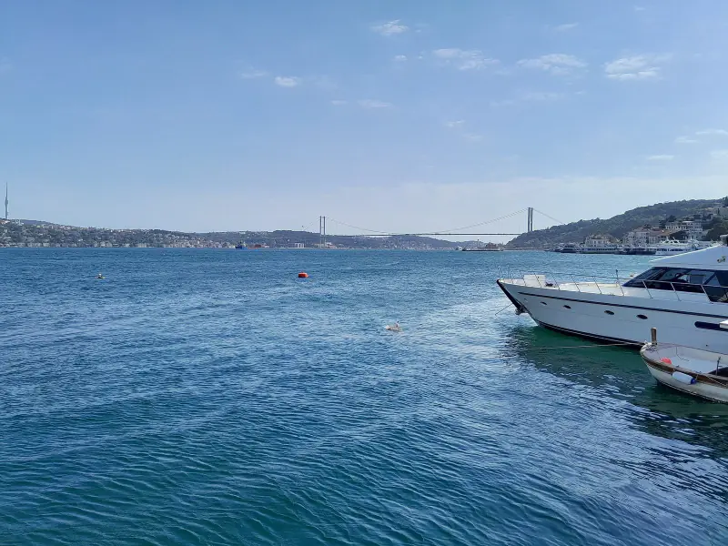 Bebek'te Boğaz kıyısı, suda bir tekne ve uzakta köprü