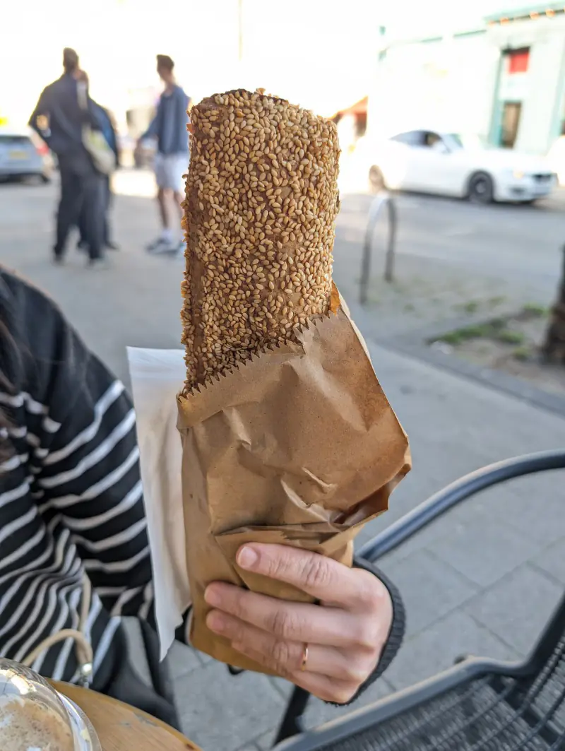 A hand holding a sesame bread ring in a paper bag